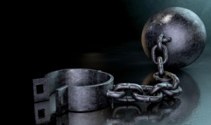 A vintage ball and chain with an open shackle on a dark backlit studio background